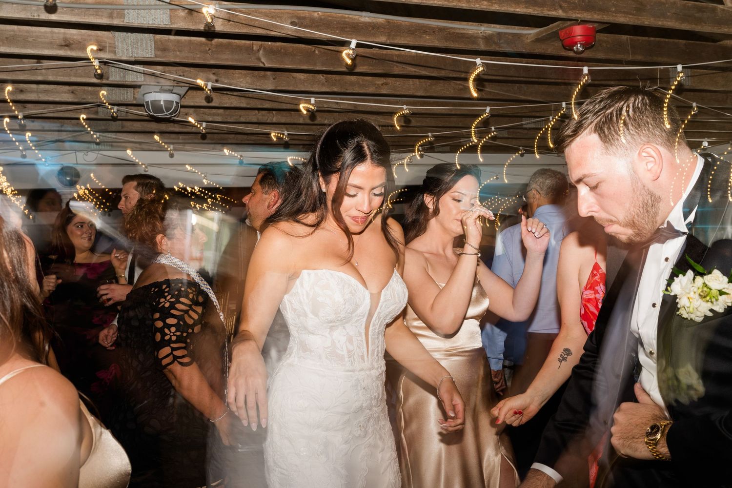 Bride in white lace gown dancing joyfully with guests at a lively wedding reception celebration.