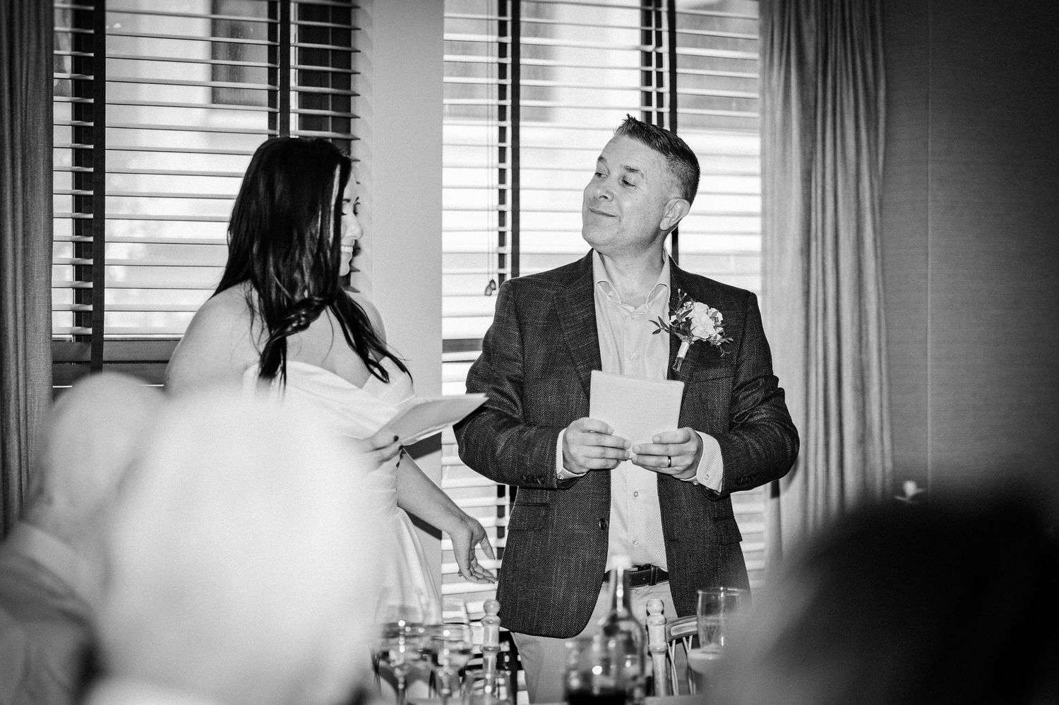 Black and white wedding photo of bride and groom exchanging vows at elegant indoor reception.