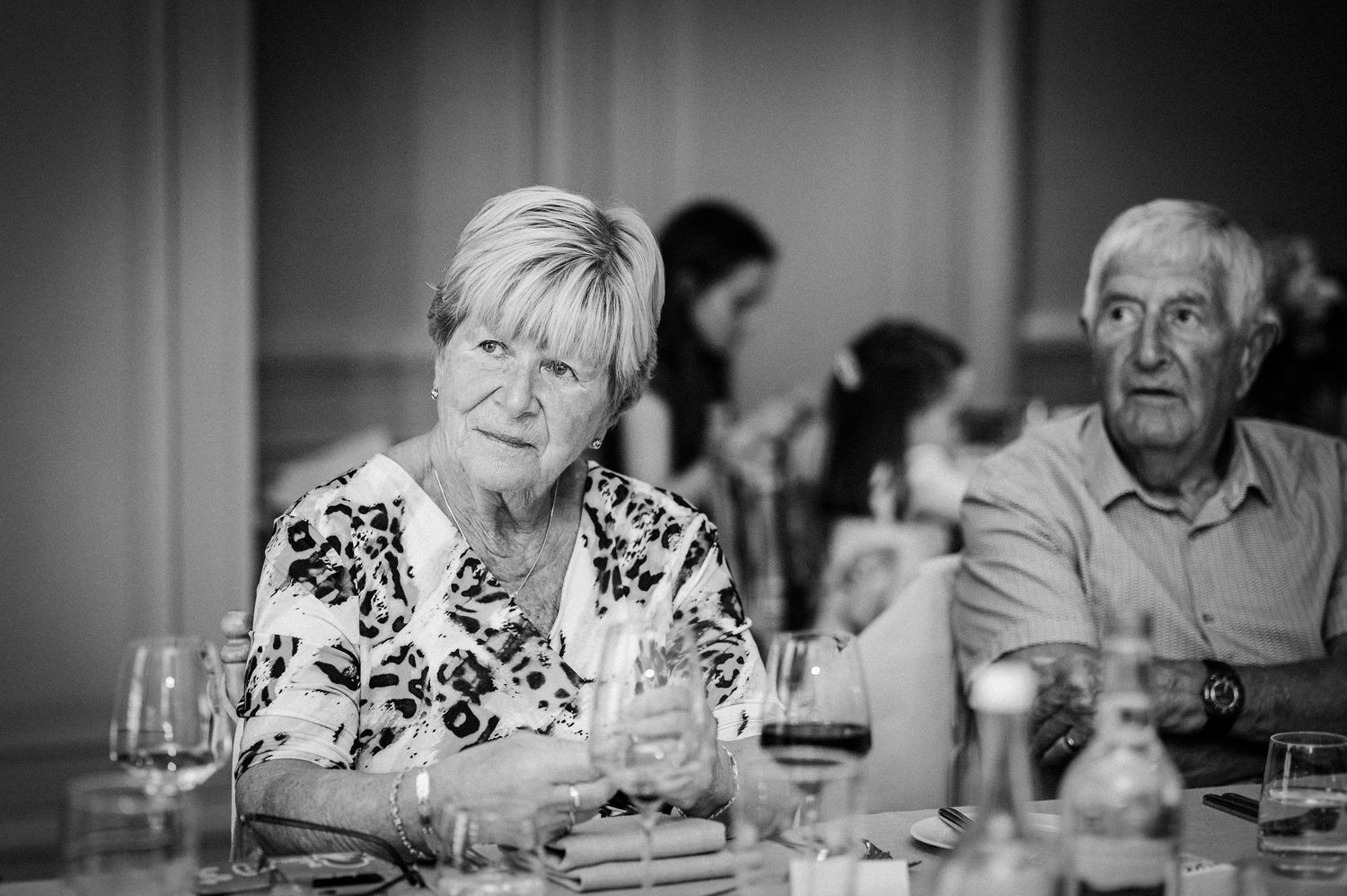 Elderly couple seated at a formal dinner table in black and white photography.