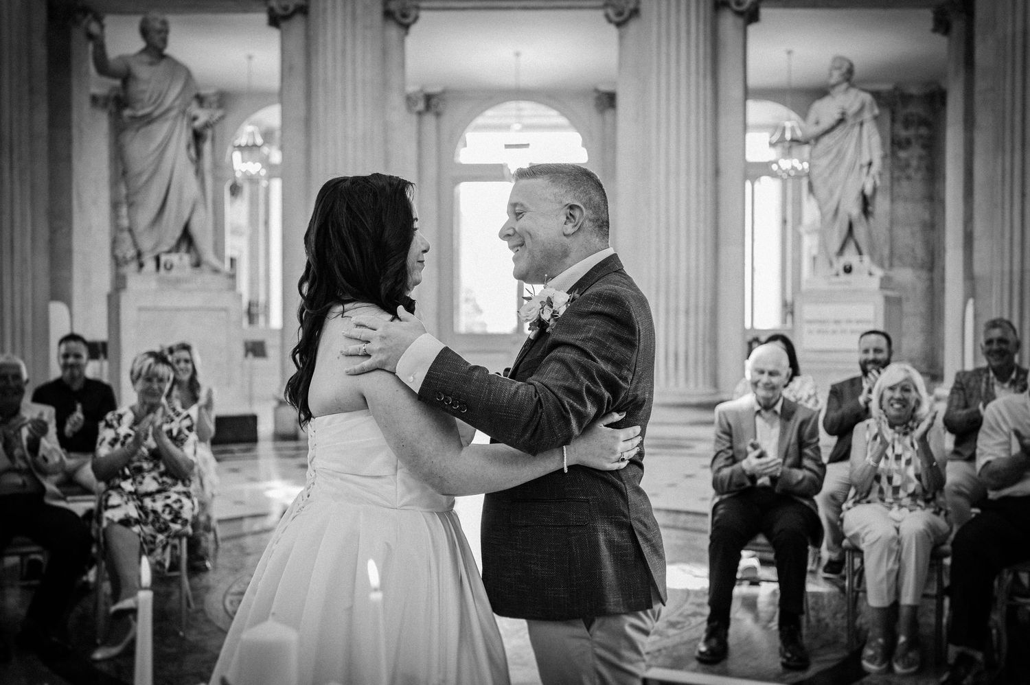 Bride and groom share first dance at elegant wedding ceremony with guests seated in ornate hall.