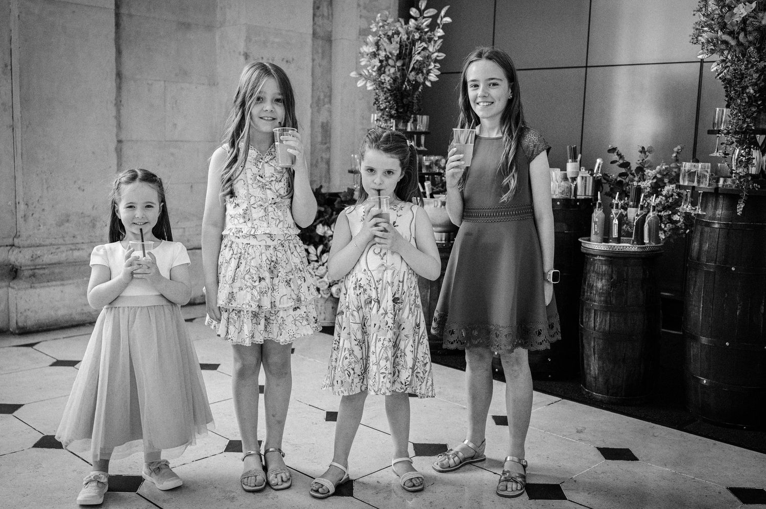 Four young girls in dresses sipping drinks at a formal event in a black and white photo.