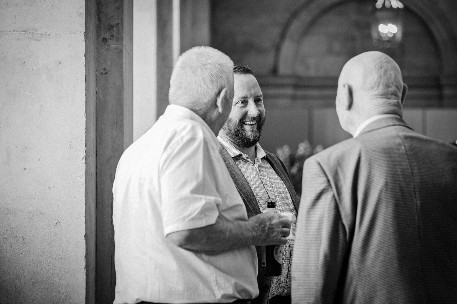Black and white photo of three men socializing and laughing at a formal event or wedding reception.