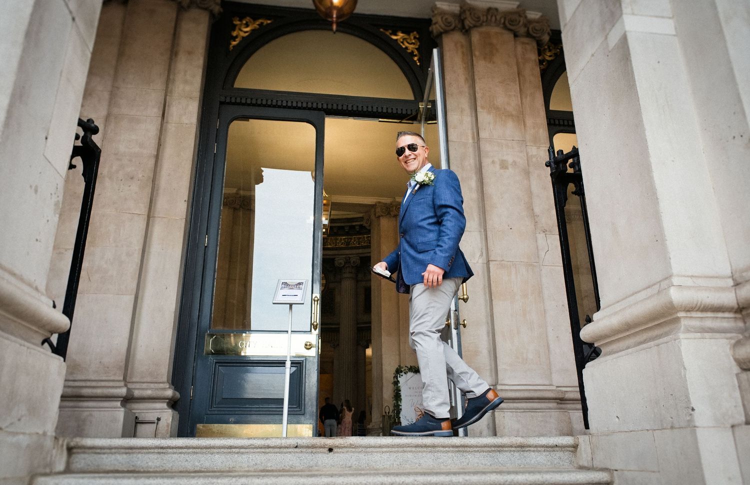 Stylish man in blue blazer and sunglasses descending grand stone steps of a classical building.