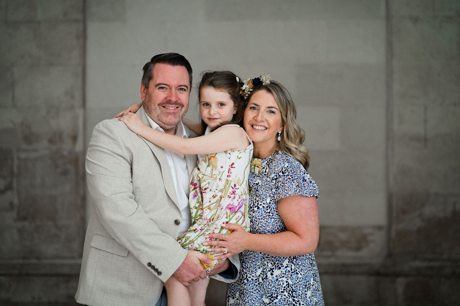Happy family portrait with father, mother, and young daughter posing together indoors.
