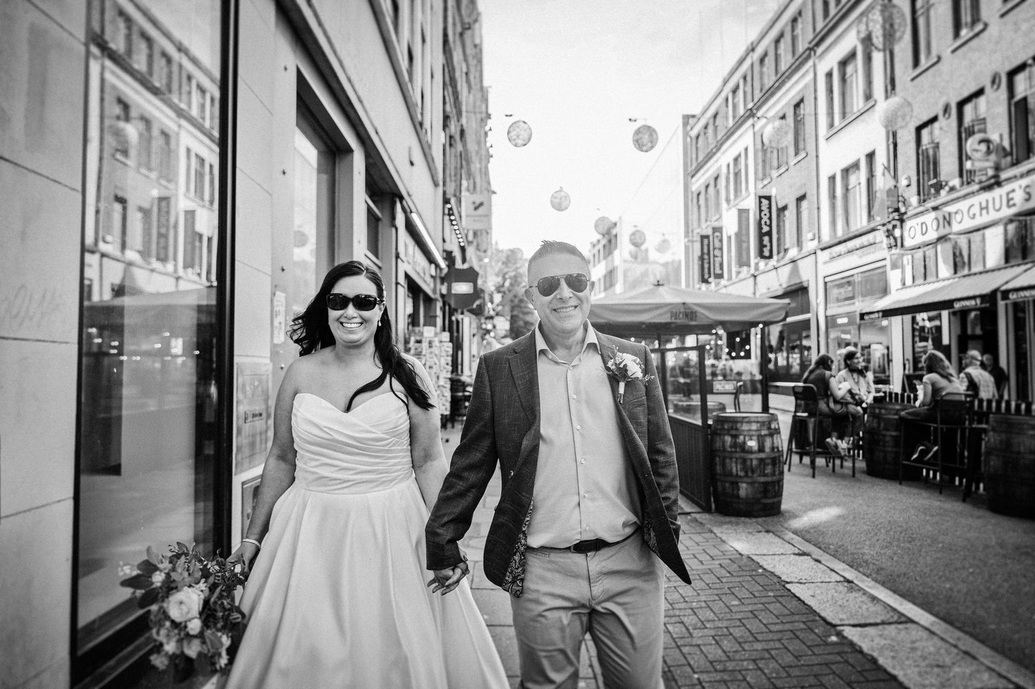 Bride and groom holding hands walking down a charming city street in black and white wedding photo.