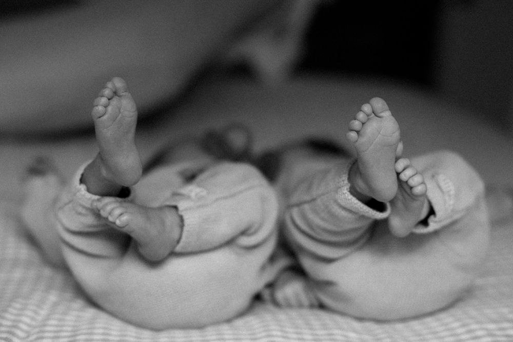 Black and white photo of newborn twins lying side by side with tiny feet raised in the air.