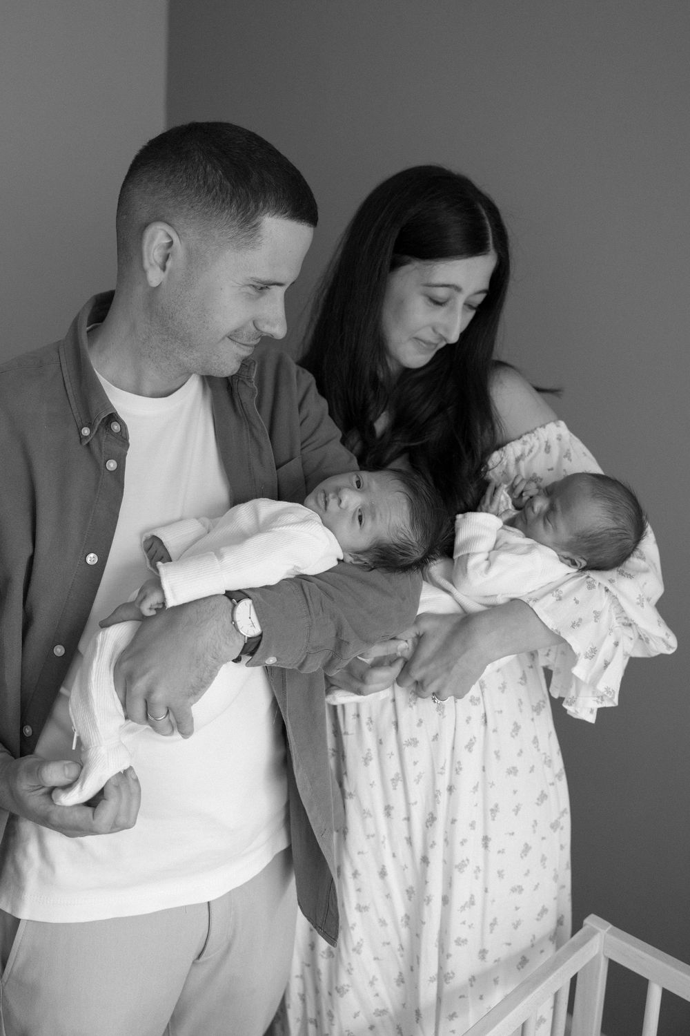 Black and white photo of parents lovingly gazing at their newborn twins, cradled in their arms.