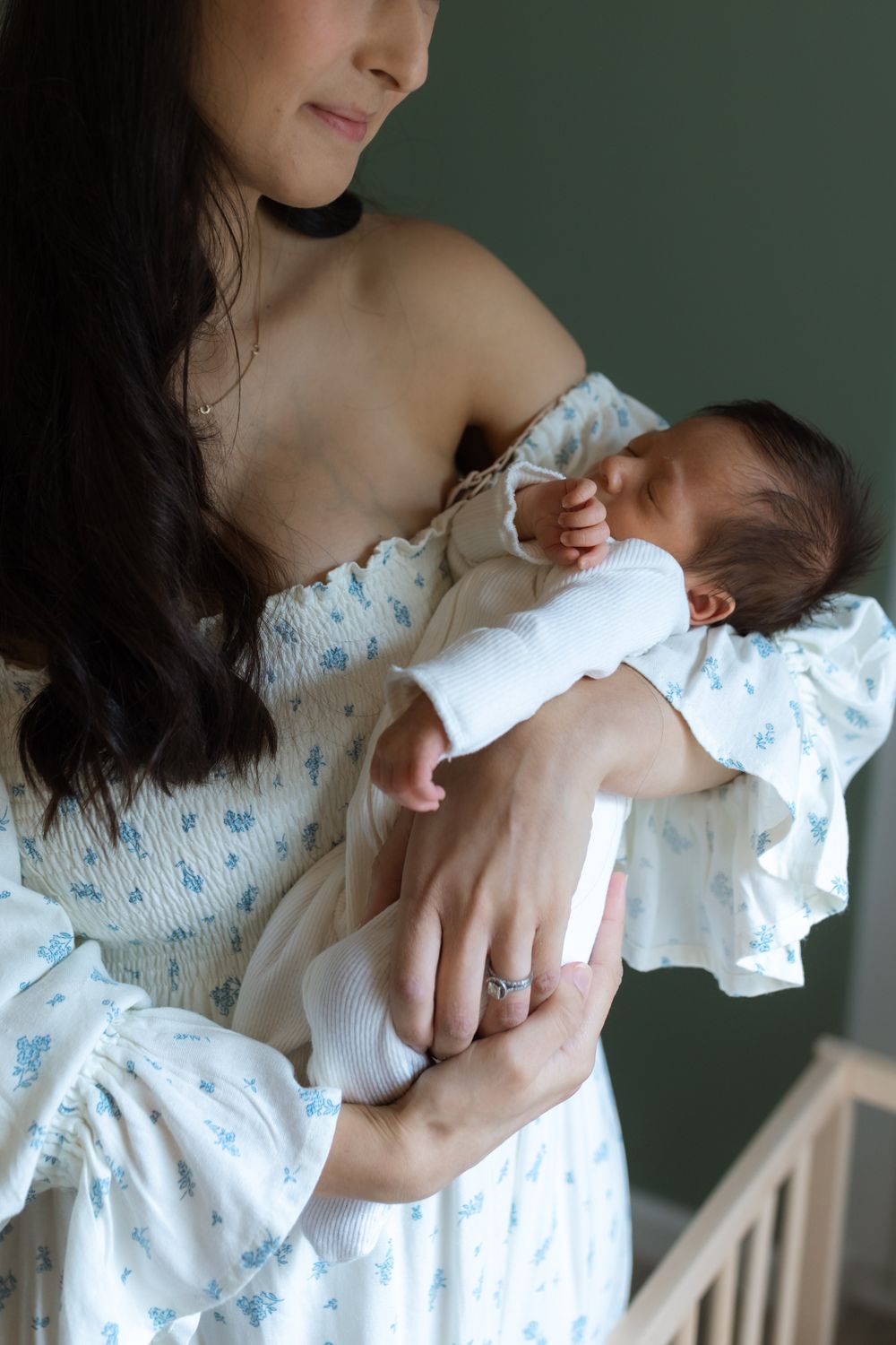 A mother in a floral dress tenderly holds her sleeping newborn baby wrapped in white.
