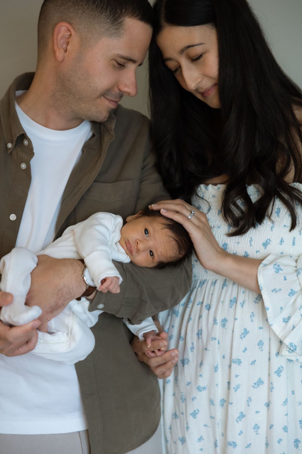 A couple tenderly gazes at their newborn baby, with the mother gently touching the infant's head.