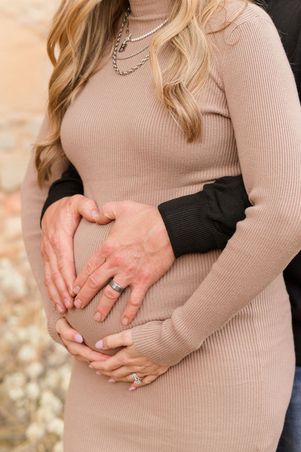 Close-up of couple's hands forming heart shape on pregnant belly, woman wearing engagement ring.