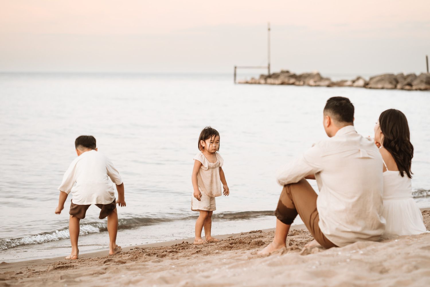 Family of four enjoying a peaceful beach sunset, with two young children playing by the water's edge.