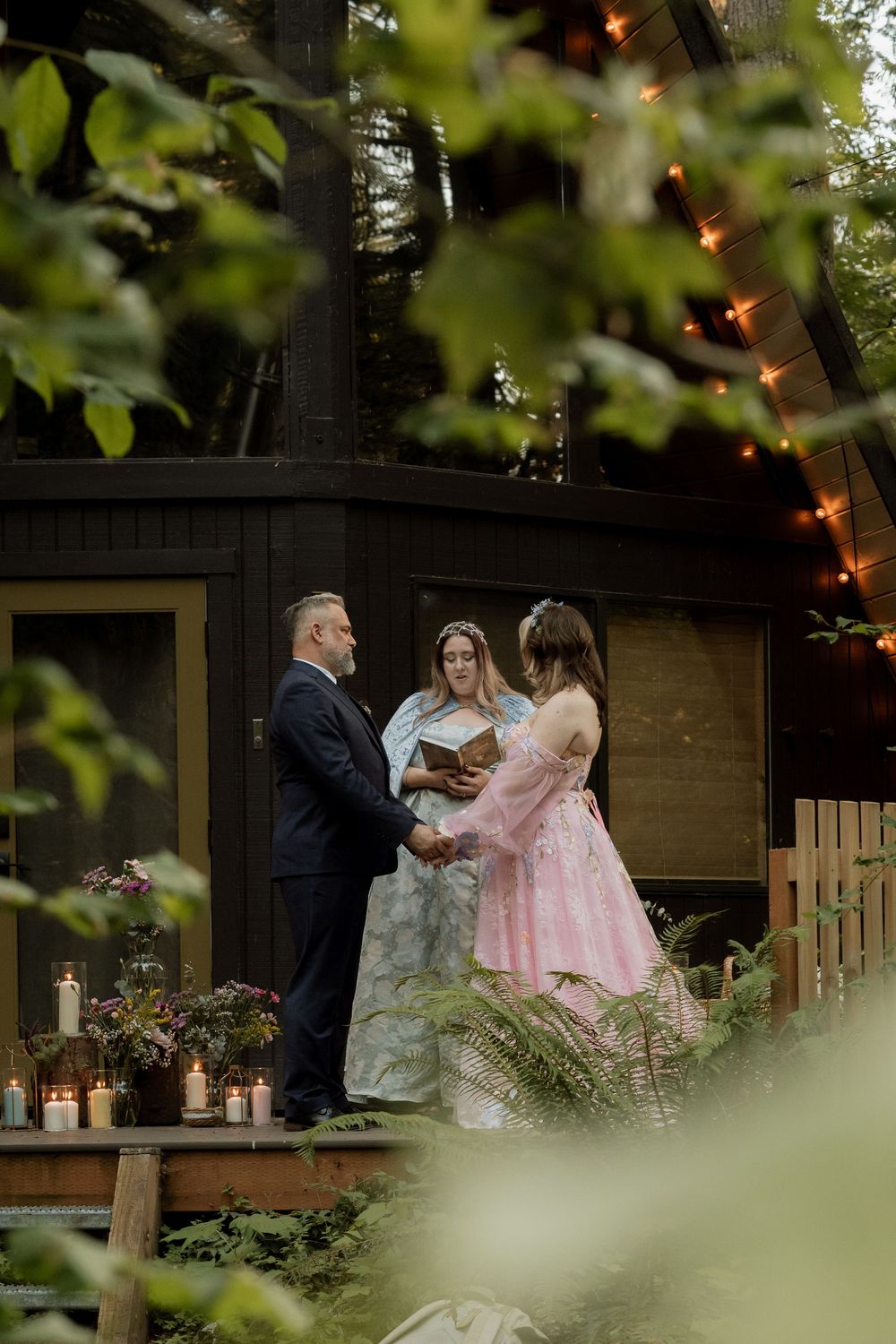 Couple exchanging vows at an outdoor woodland wedding ceremony with string lights and candles.