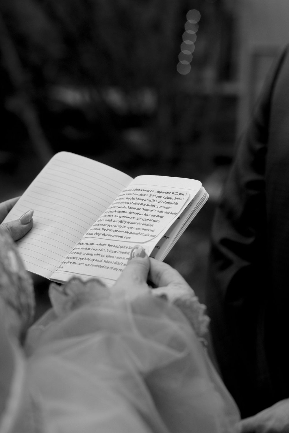 Black and white photo of hands holding an open notebook with handwritten wedding vows during a ceremony.