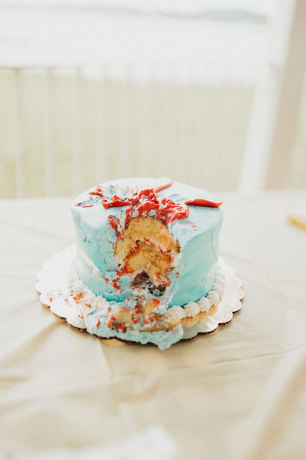 A partially eaten smash cake with light blue frosting and red decorations on a white doily.
