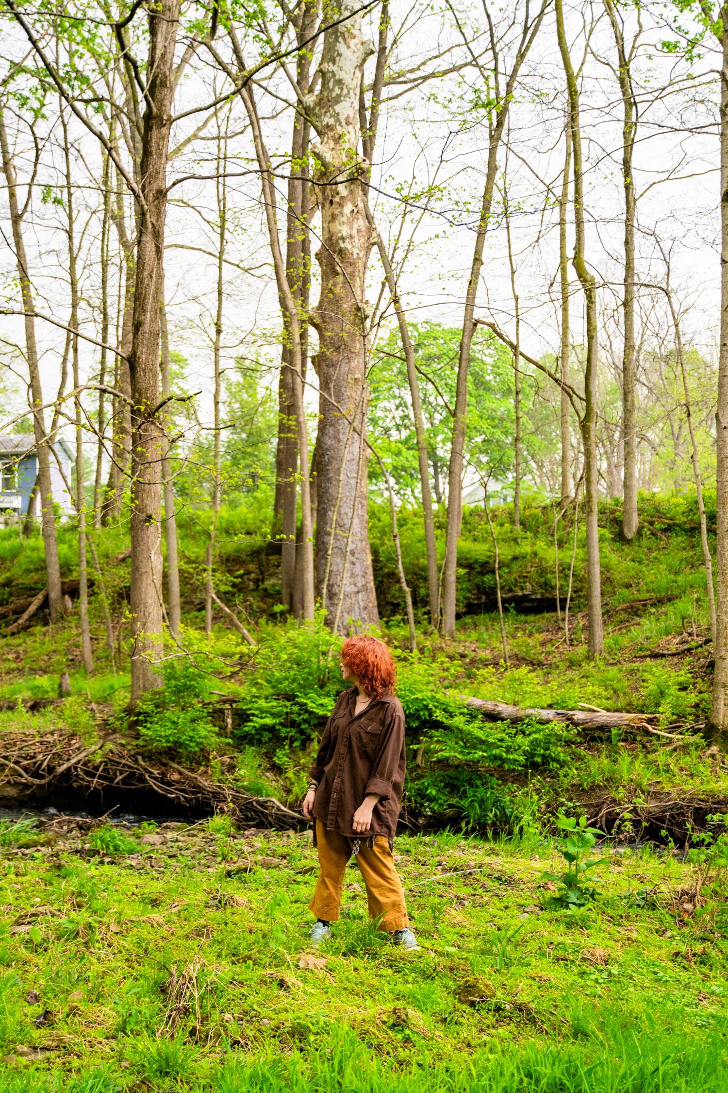 Person with red hair standing on stairs in a hallway with brick walls, wooden doors, and posted flyers.