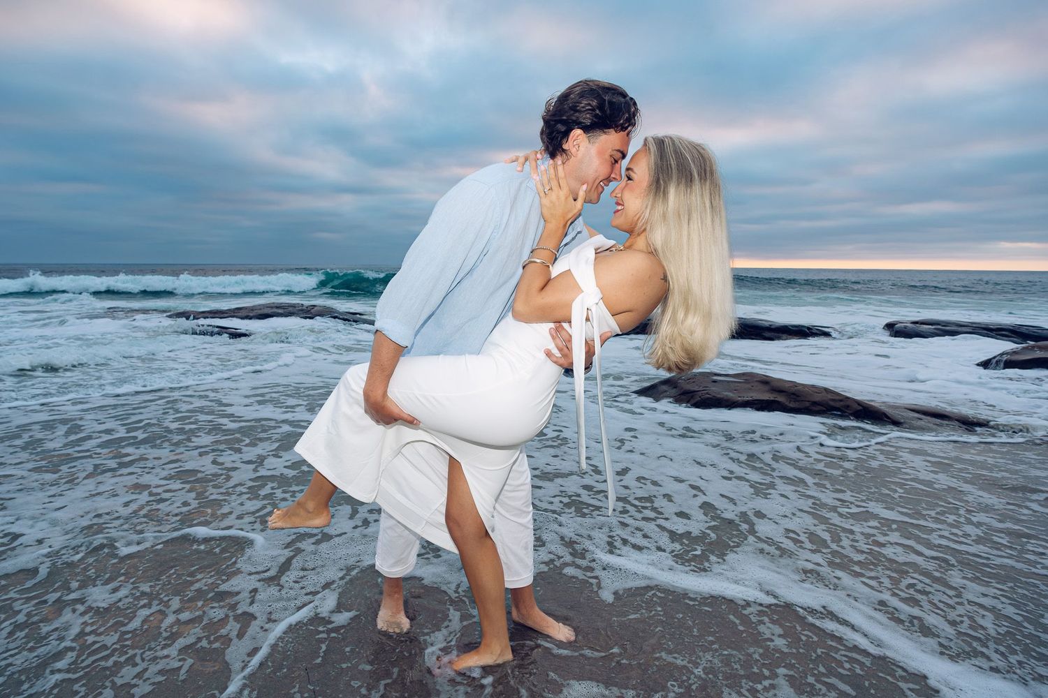 Surprise wedding proposal in La Jolla, San Diego featuring a newly engaged couple embracing on the beach as waves crash behind them.