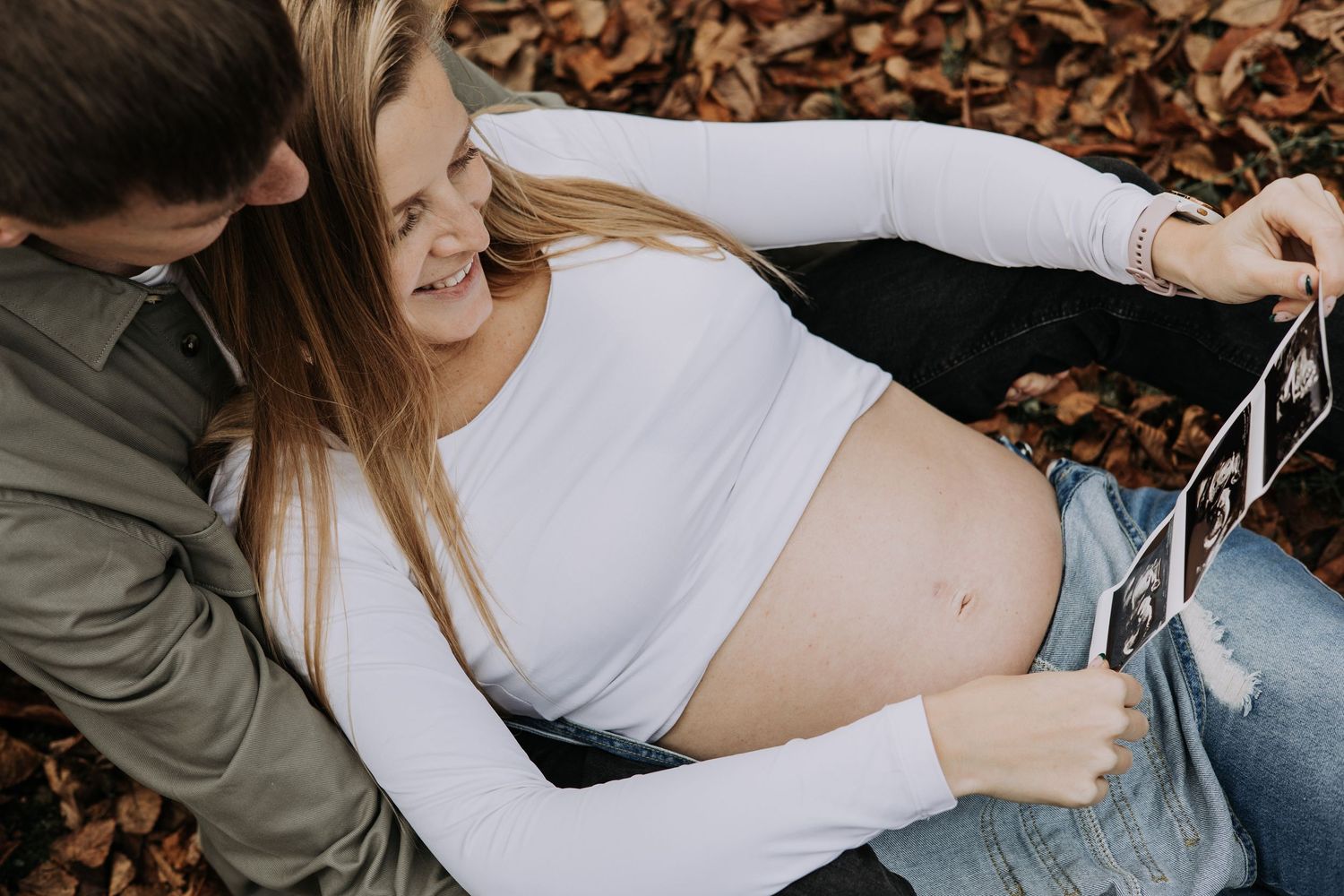 Pregnant woman sitting outdoors with her partner while looking at ultrasound scan photographs.
