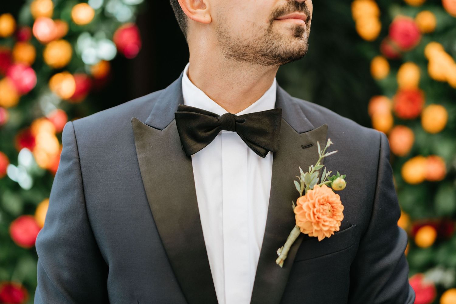 Portrait of groom Sina wearing a black tuxedo with an orange floral boutonniere before the ceremony.
