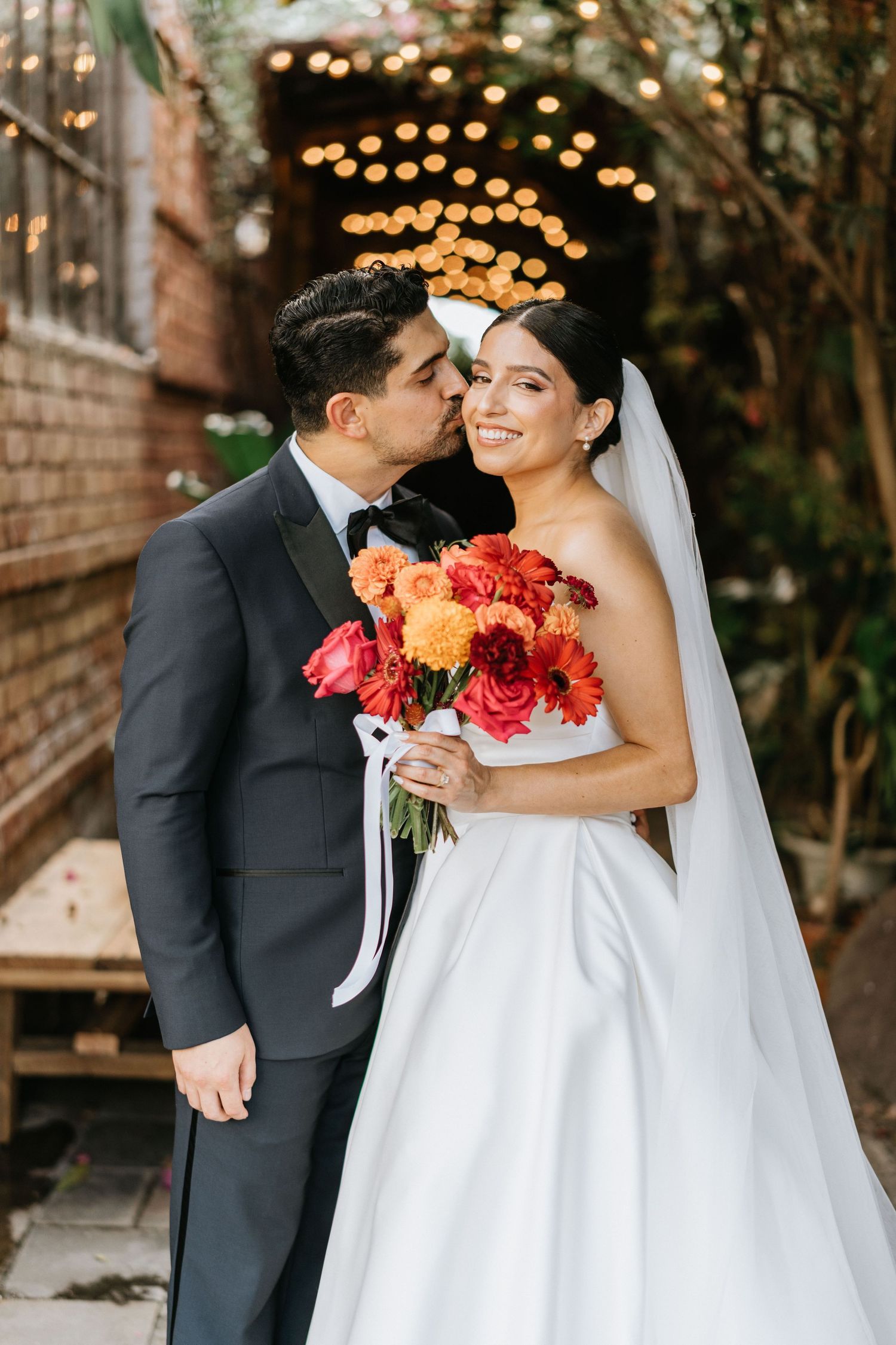 Ruby and Sina embracing beneath string lights during romantic wedding portraits.