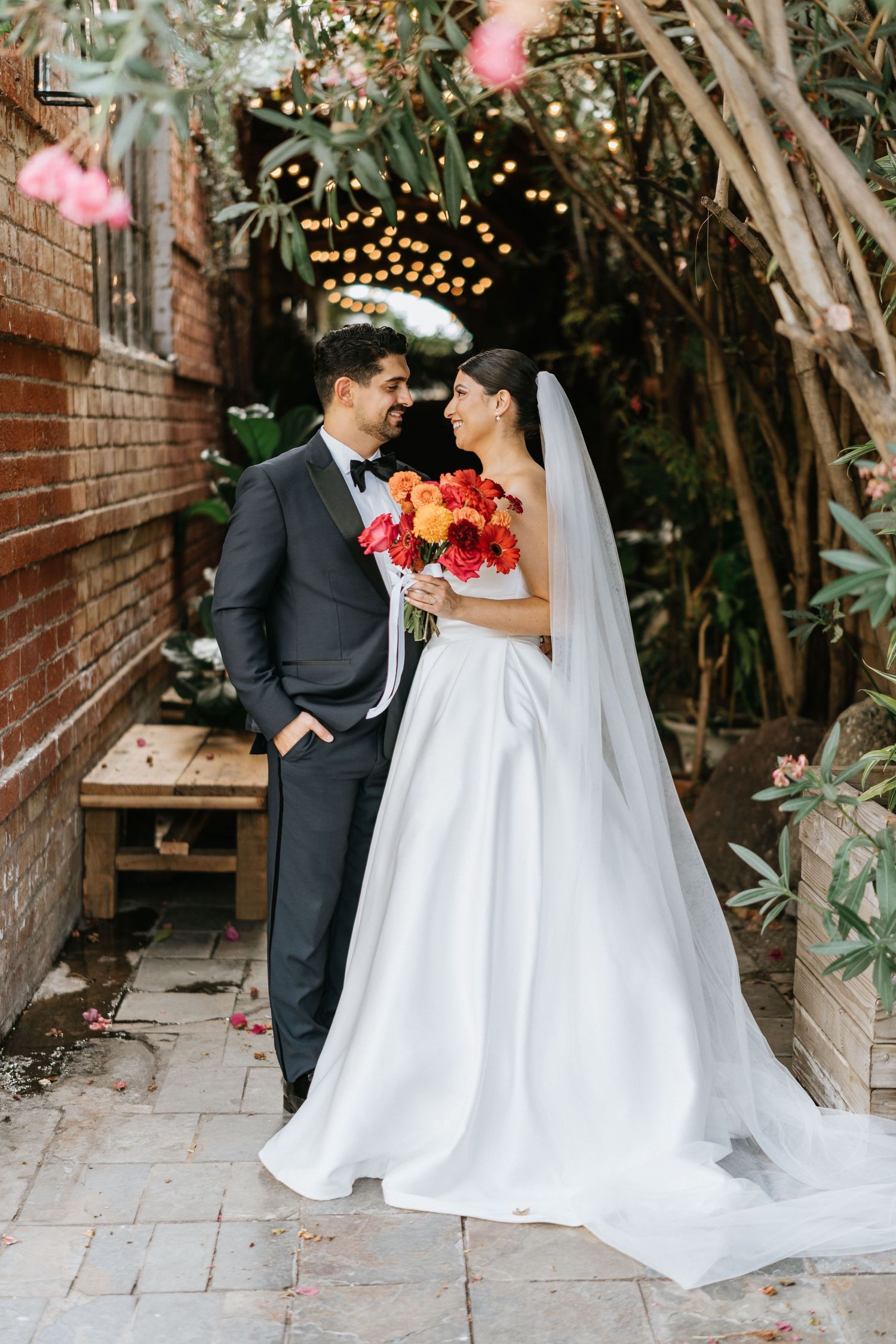 Ruby and Sina sharing a kiss beneath string lights after their wedding ceremony.