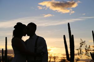 Silhouette of a couple kissing against a colorful desert sunset sky with tall saguaro cacti in the background.