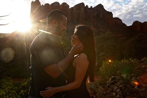 Silhouetted couple embraces in golden sunset light with sun flare in front of towering red rock formations in Sedona.