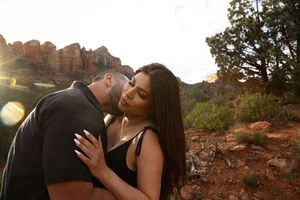 Man and woman share an intimate kiss at golden hour with red rock buttes and green shrubs behind them.