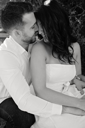 Black and white portrait of a couple embracing as the man kisses the forehead of a woman in a white strapless dress.