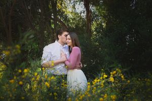 Romantic engagement portrait of a couple hugging in a lush garden surrounded by bright yellow flowers.
