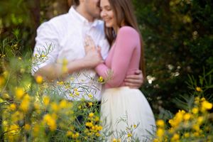 Close-up of a couple embracing among blooming yellow wildflowers, the woman in a pink top and white skirt.