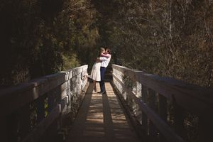 Couple embracing at the center of a wooden bridge surrounded by dark forest in a dramatic outdoor engagement photo.