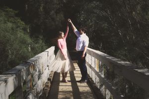Couple dancing on a wooden bridge in a forest, the woman in a flowing tulle skirt twirling under her partner's raised hand.