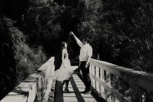 Black and white photo of a couple dancing on a wooden bridge in the woods as the woman twirls in a flowing skirt.