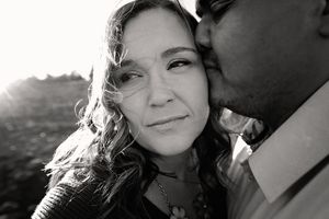 Black and white close-up portrait of a man kissing a woman's cheek as she gazes softly at the camera.