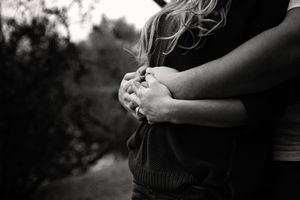 Black and white close-up of a couple's hands clasped together as a man wraps his arms around a woman with long wavy hair.