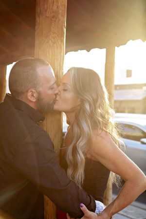 Couple sharing a romantic kiss beneath a wooden porch awning in warm golden sunset light.