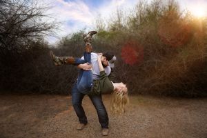 Couple posing playfully outdoors at sunset as a man dips a woman backward in a romantic engagement photo session.