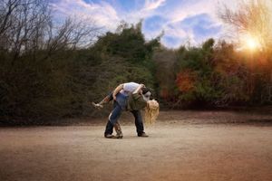 Man dips a woman in a dramatic dance pose on a dirt path surrounded by trees with warm golden sunlight behind.