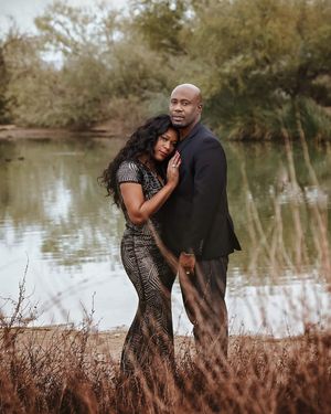 Couple in an intimate embrace beside a calm lake, the woman in a sparkling dress and the man in a dark suit.