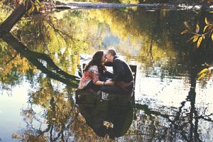 Couple kissing in a small boat on a calm lake reflecting golden autumn trees.