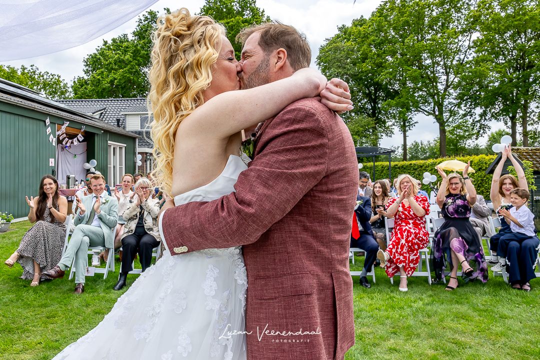 Vincent en Madelief kussen elkaar na het ja-woord, terwijl familieleden op de achtergrond klappen