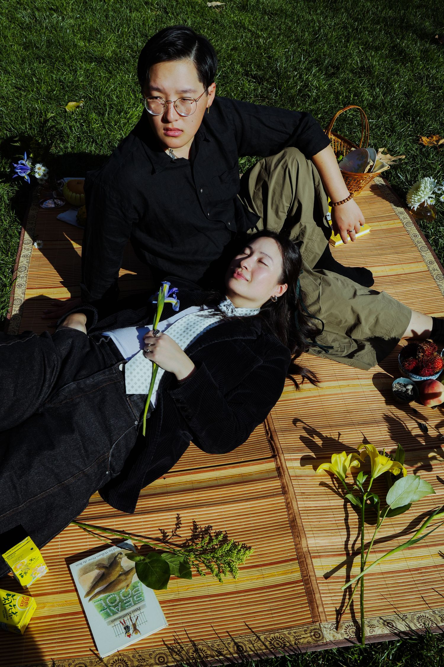 A couple picnicking in the grass, surrounded by different fruits and flowers at the Lewis MacAdams Riverfront Park in Los Angeles.
