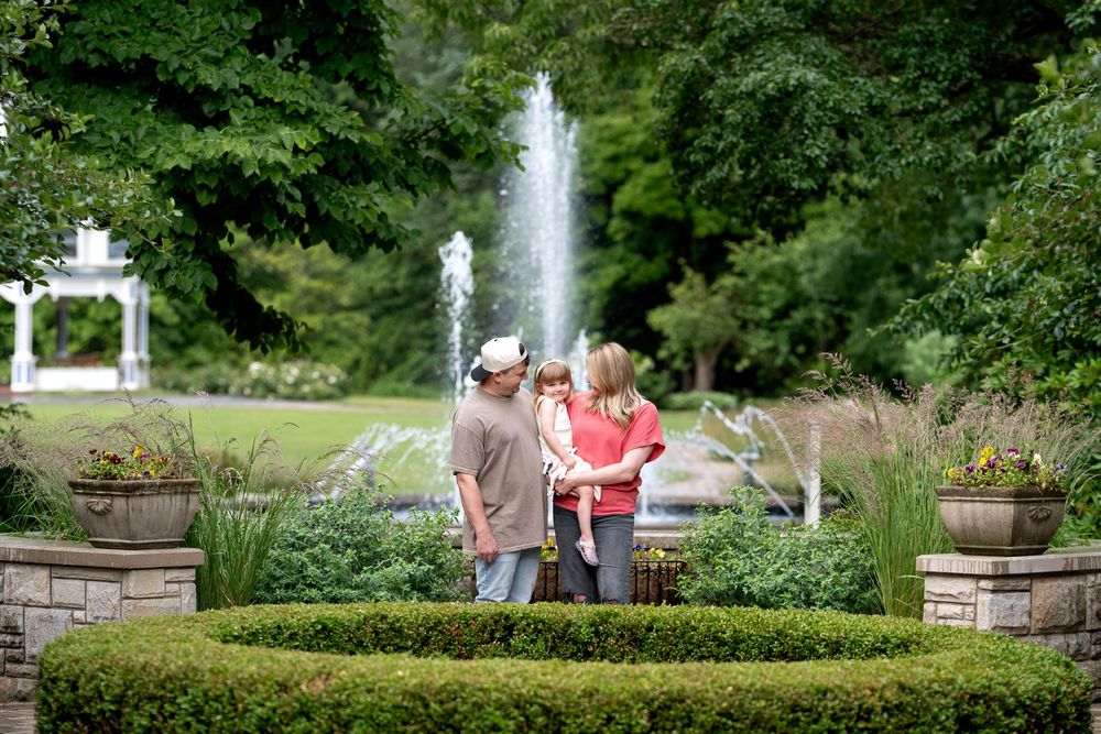 Family enjoying a lush garden with a fountain and green hedges on a sunny day.