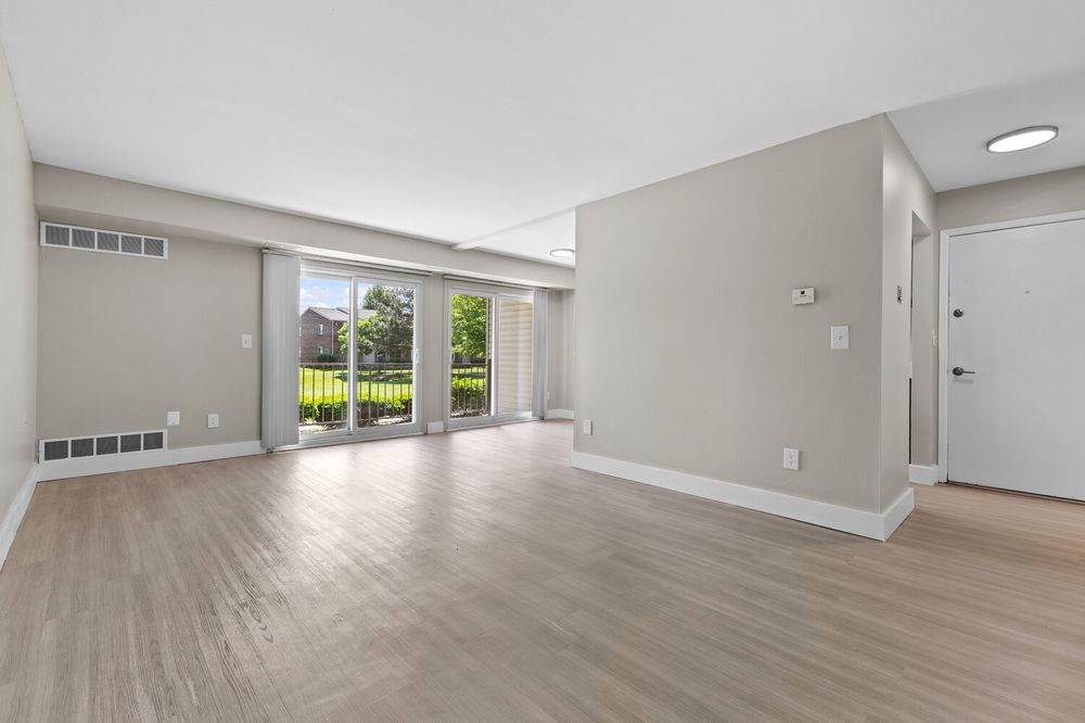 Bright open living area with light hardwood floors, sliding glass doors to patio, and neutral gray walls.