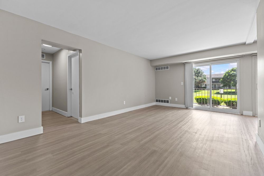 Bright open living room with light hardwood floors, sliding glass door, and view of green outdoor space.