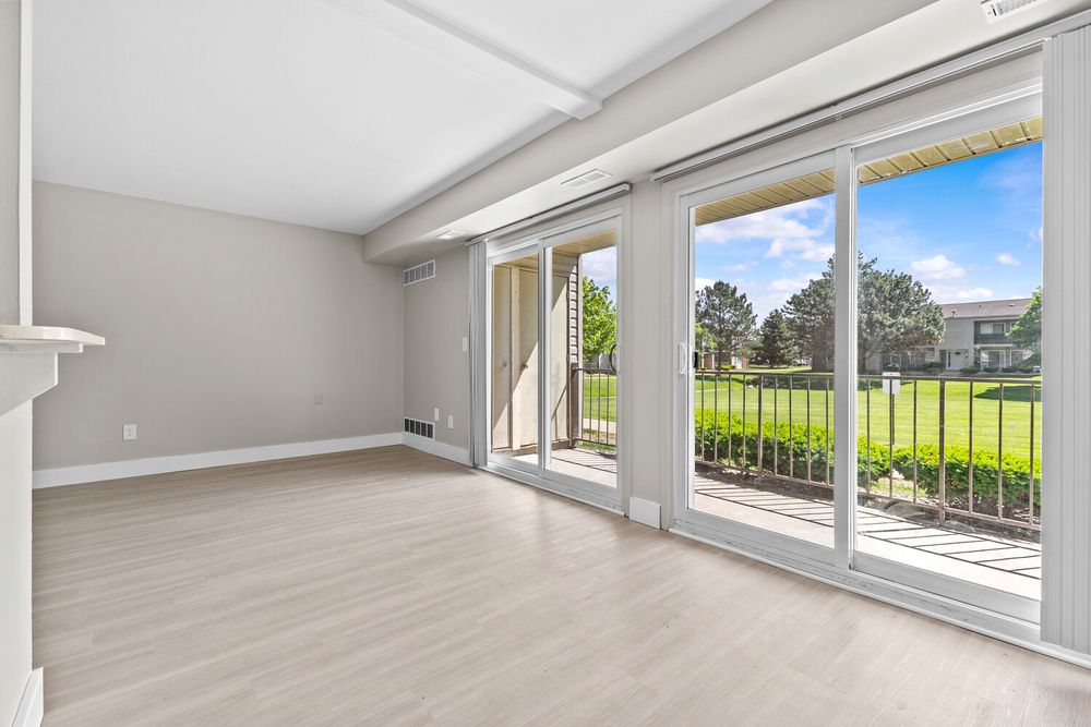 Bright living room with large sliding glass doors opening to a green backyard, light hardwood floors, and neutral gray walls.