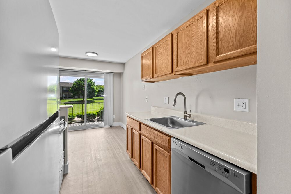 Modern kitchen with oak cabinets, stainless steel dishwasher, sink, and sliding door to outdoor deck.