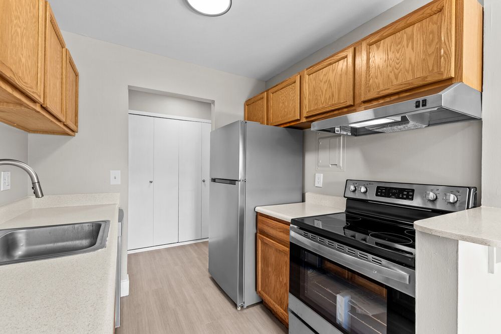 Modern kitchen with stainless steel appliances, oak cabinets, and light wood flooring in a bright apartment.