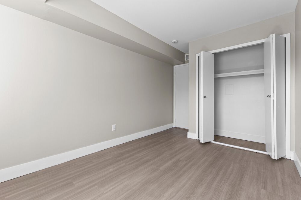 Empty bedroom with open bifold closet doors, light gray walls, and modern laminate hardwood flooring.