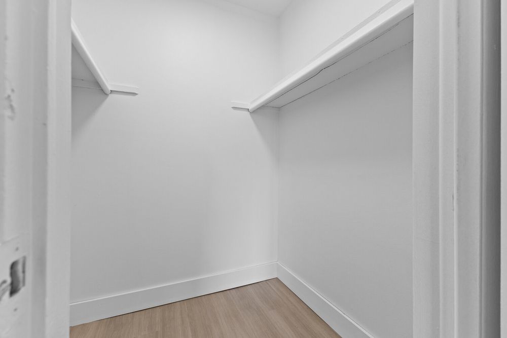 Spacious walk-in closet with white walls, built-in shelving, and light hardwood flooring in a modern home.